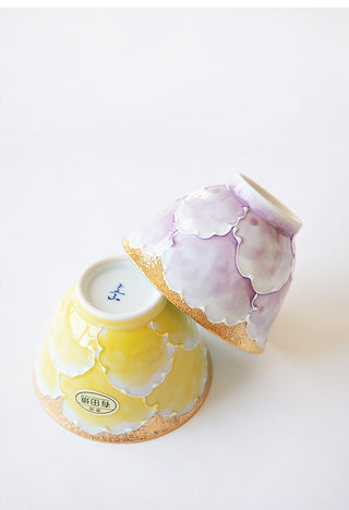 Two handmade ceramic bowls with a glossy glaze, one in pastel yellow and the other in pastel lavender, displayed upside down on a clean white background.