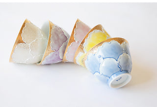 Four hand-painted ceramic tea cups arranged in a fan shape on a clean white background, each featuring a different pastel color and a gold hand-painted border.