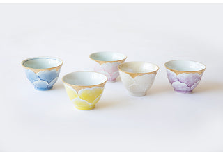 Five small ceramic cups arranged on a clean white background, each with a different pastel body color and a metallic gold rim.