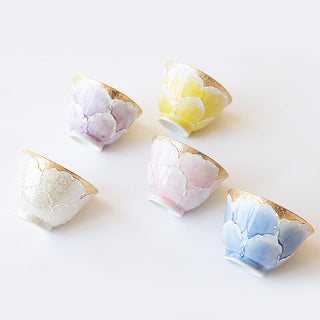 Five small ceramic cups with a glossy hand-painted lotus flower pattern in pastel shades of purple, yellow, pink, white, and blue, each finished with a gold leaf pattern on the rim, arranged on a clean white background.