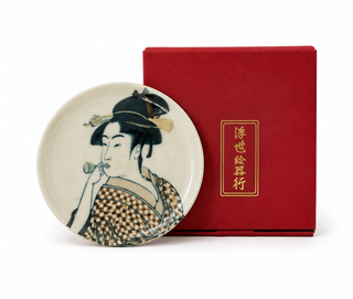 A round ceramic plate featuring a traditional Japanese geisha illustration, displayed next to its red presentation box with gold Chinese characters on a white background.